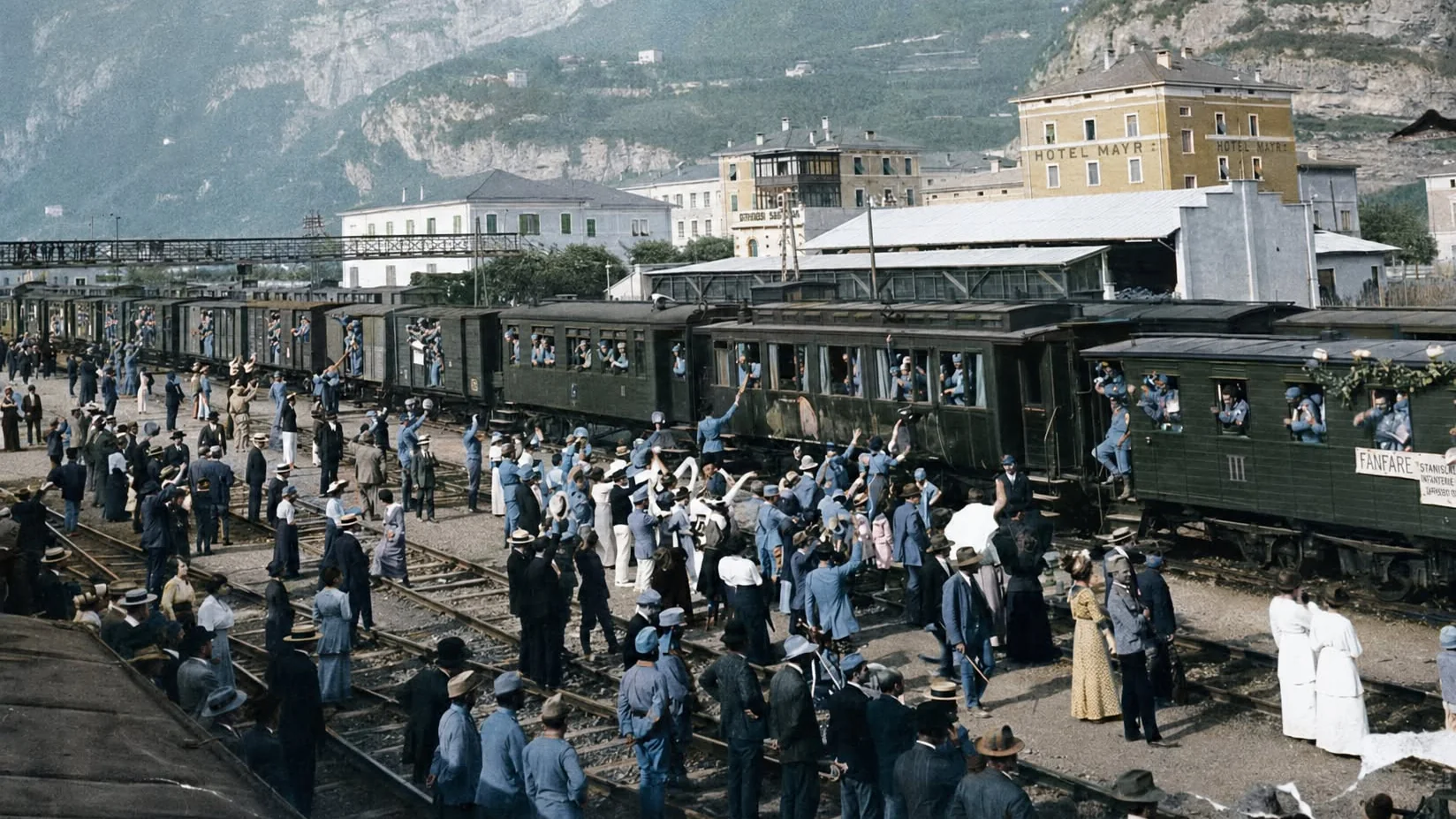 Soldati in divisa austro-ungarica salutano dai vagoni di un treno affollato mentre la folla li accompagna, stazione ferroviaria, 1914.